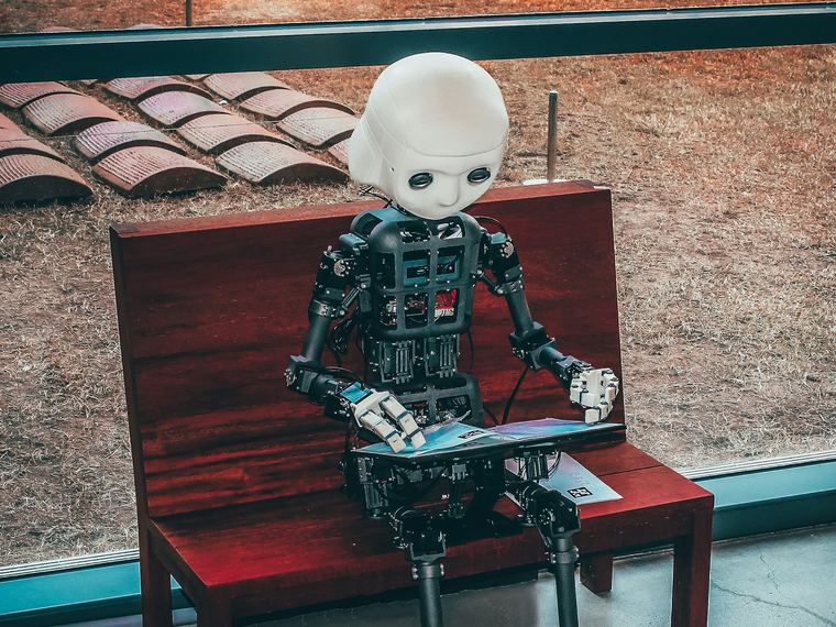 Mensvormige robot die zittend op een bankje een tijdschrift leest